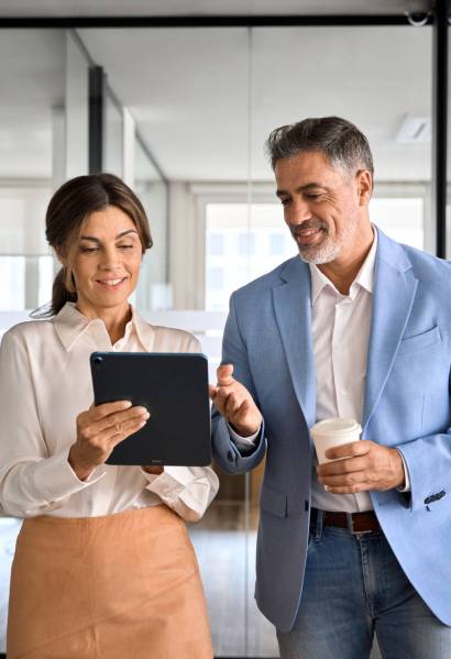 Two busy business man and woman executives team using tablet in office. Busy mature professional business people, two happy business man and woman executives partners team working together walking in office using digital tablet talking on company financial project.